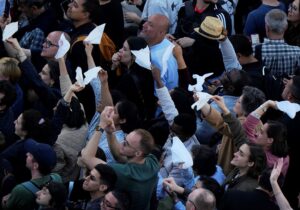 People react as white smoke appears from the chimney of the Sistine Chapel where 133 cardinals gathered on the second day of the conclave to elect a successor to late Pope Francis, at the Vatican, on May 8, 2025.
